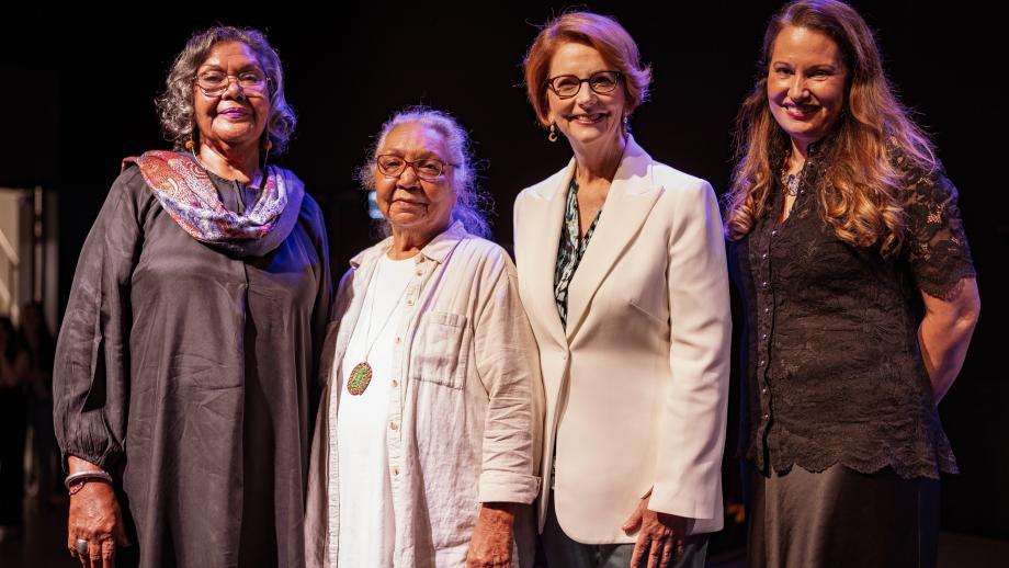 Four women stand on a stage looking into the camera.