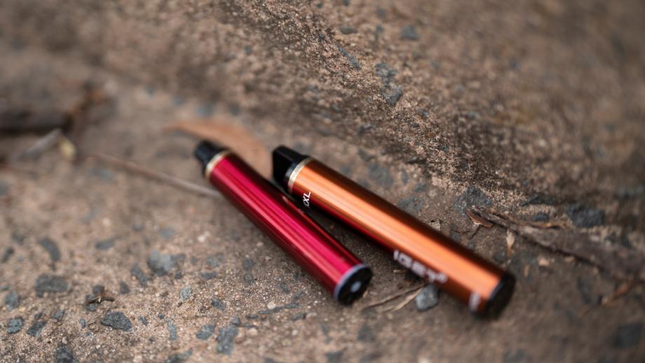 Two e-cigarettes (one red, one orange) discarded on the ground. 