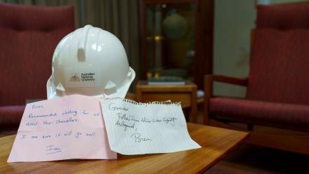 A hard hat on a table, with two handwritten notes placed in front of it.