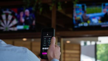 A person holds up their phone while watching a sporting match on TV.