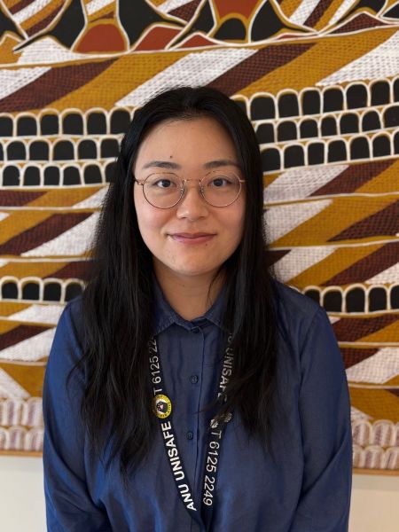 A woman standing in front of a painting with long dark hair and a blue shirt