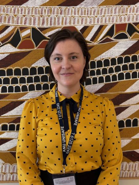 A woman with short dark hair standing in front of a painting wearing a yellow shirt
